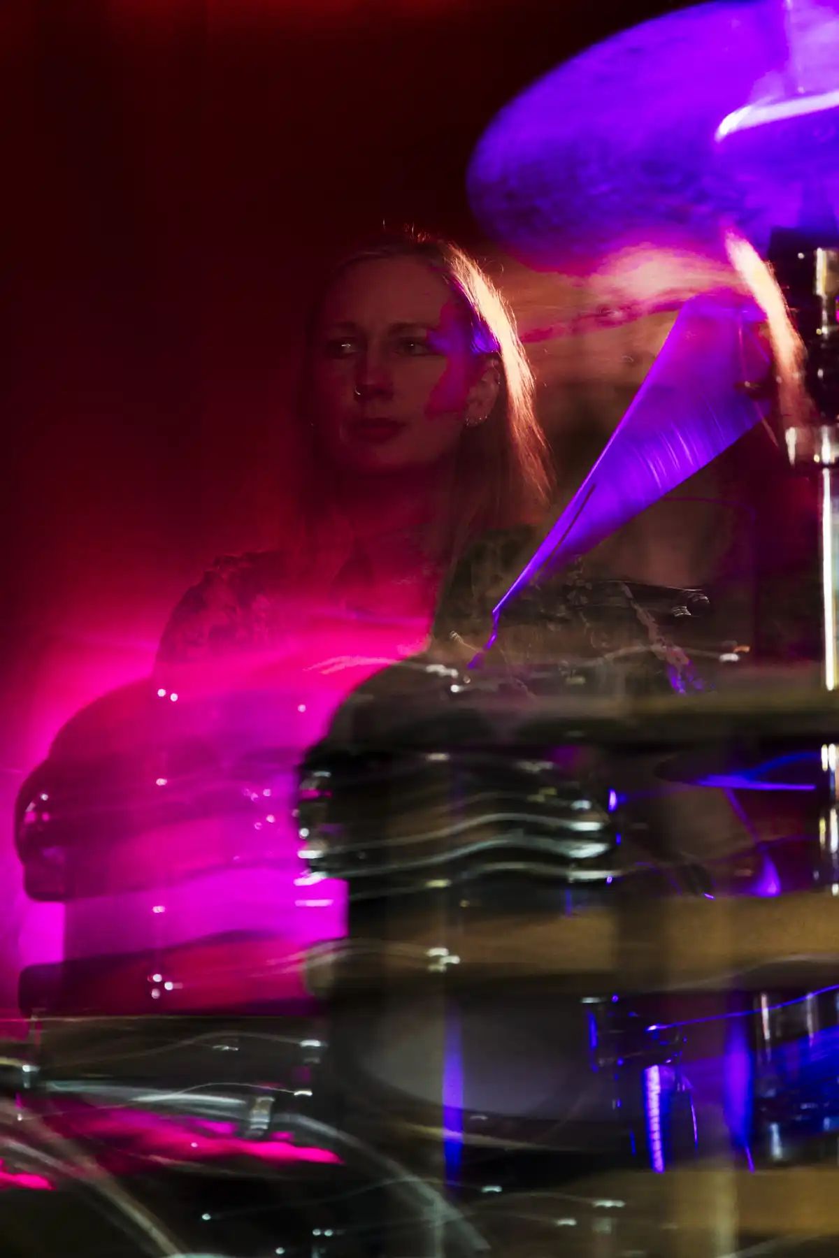 A blurry, red and purplish photo of me at a drumkit