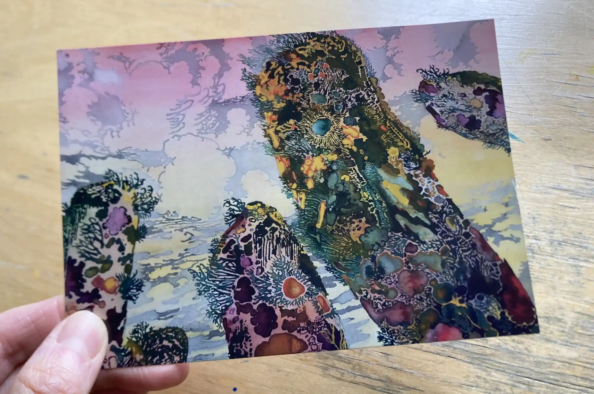 Hand holding a postcard of a colourful painting