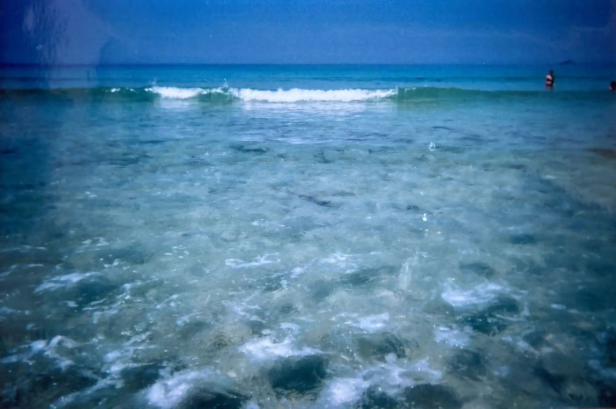 An old photo looking out to sea with a blue sky and a wave approaching