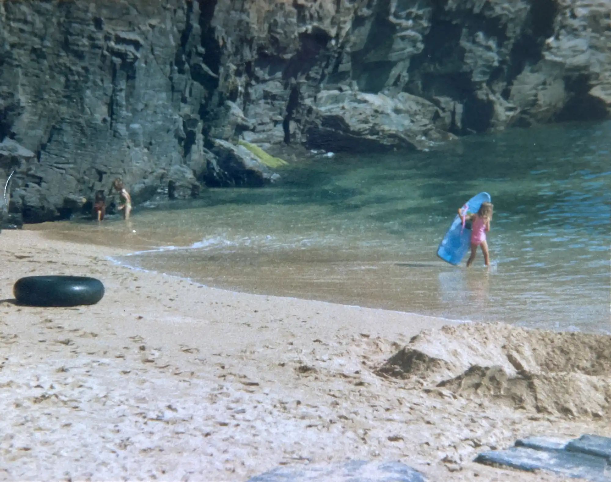An old photo of a child heading into the sea with a blue foam surfboard